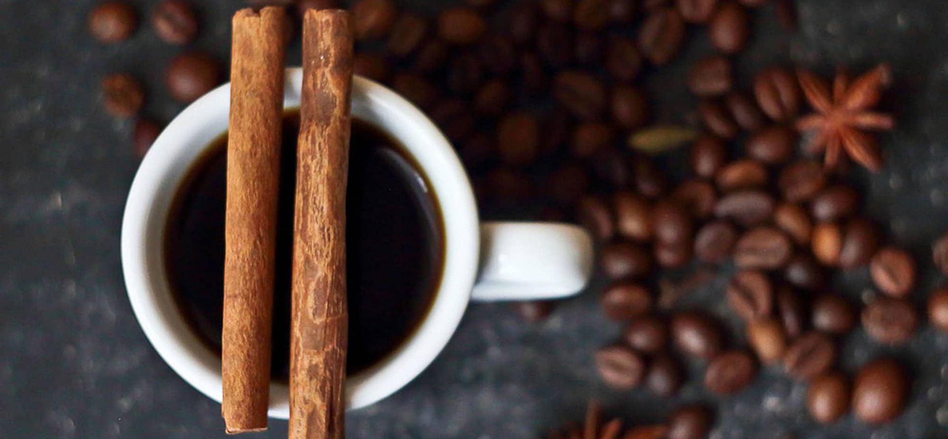 A cup of coffee with cinnamon sticks and coffee beans.