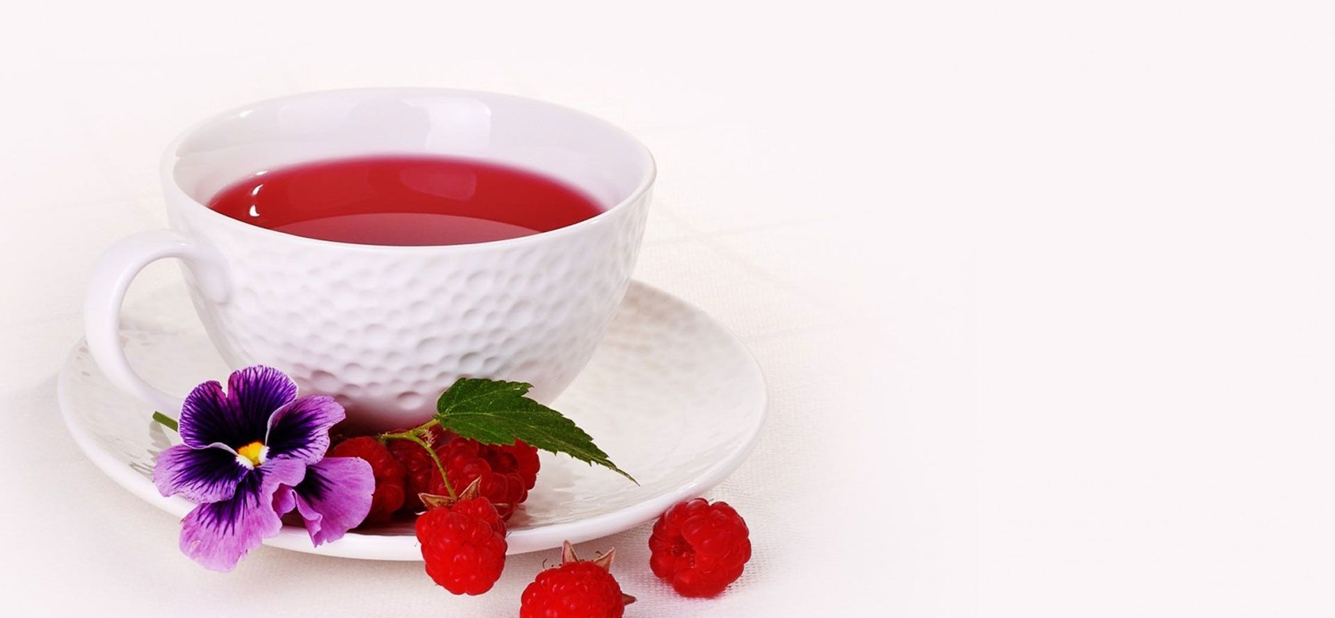 White cup with red raspberry tea on white background